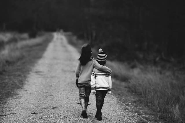Two children walking together down a country path, arms around each other
