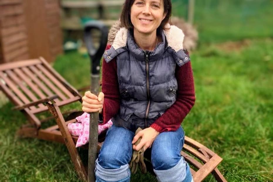 Woman in pink wellies holding a spade and smiling at allotment — wildlife gardening for wellbeing